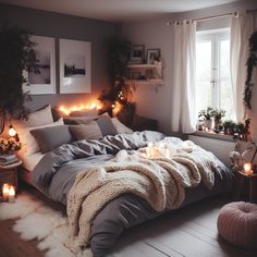 an unmade bed with blankets and candles on the floor in front of a window