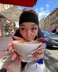 a woman drinking from a white cup on top of a table