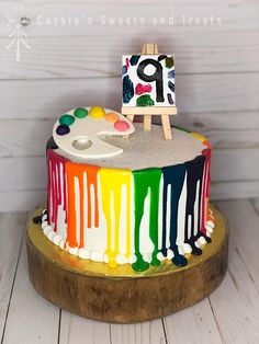 a multicolored cake with an easel and paint splattered on it