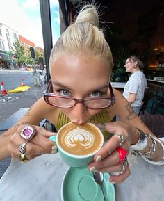 a woman with glasses is drinking from a coffee cup in front of her face and looking at the camera