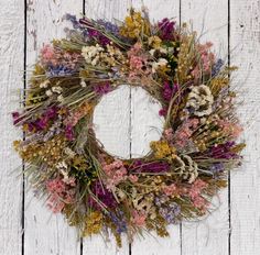 a dried wreath is hanging on a white wooden wall with purple, yellow and pink flowers