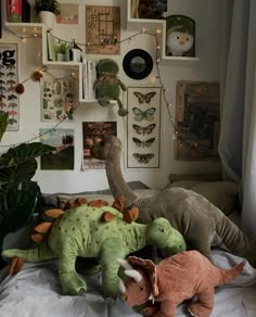 two stuffed dinosaurs sitting on top of a bed next to a wall full of pictures