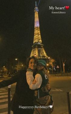 two people taking a selfie in front of the eiffel tower at night