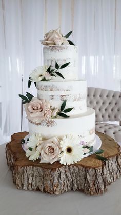 a three tiered cake with flowers on the top is sitting on a tree stump