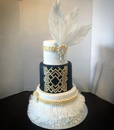 a three tiered cake with white feathers on top and gold trim around the edges