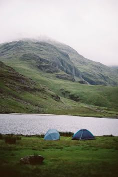 two tents pitched up next to a body of water with mountains in the back ground