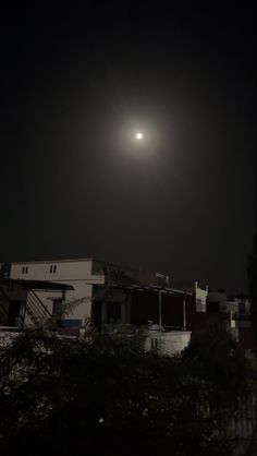 the moon is shining in the dark sky over some buildings and trees at night time