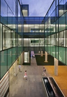 people are walking around in an open area with glass walls and water feature on the floor