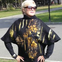 a woman with blonde hair and sunglasses standing in the grass wearing a black shirt that has yellow paint on it