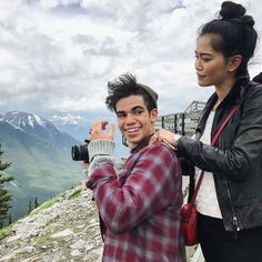 a man and woman taking pictures on top of a mountain