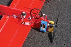 a small red airplane sitting on top of a tarmac next to a pair of scissors