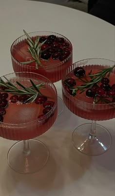 three glasses filled with red wine and garnished with cranberries on a table