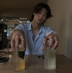 a woman holding two jars with liquid in them on a table next to a cell phone