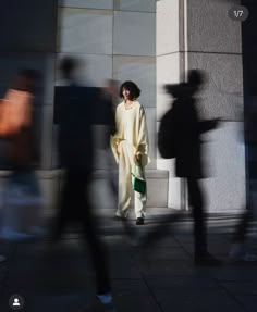 a woman standing in front of a building with her shadow cast on the wall behind her