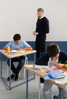 three boys are sitting at desks with books and pencils in front of them