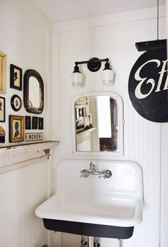 a white sink sitting under a mirror next to a black and white wall mounted clock