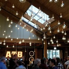 a large group of people standing in a room with lots of lights hanging from the ceiling