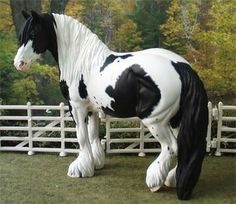 a statue of a black and white horse standing in front of a fence with trees behind it