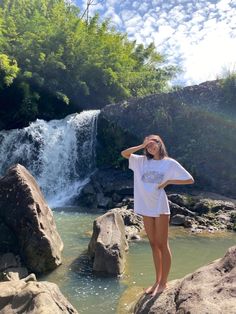 a woman standing on rocks in front of a waterfall