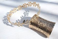 a gold bracelet with leaves on it sitting on top of a white table next to a plant