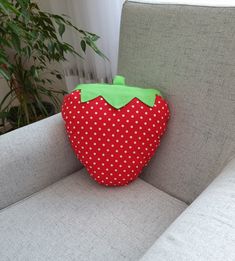 a red strawberry pillow sitting on top of a gray couch next to a potted plant