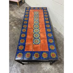 an orange and blue table sitting on top of a cement floor next to a wall