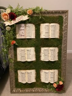 an arrangement of seating cards is displayed in a frame with moss and flowers on it