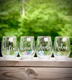 four wine glasses sitting on top of a wooden table in front of some green trees