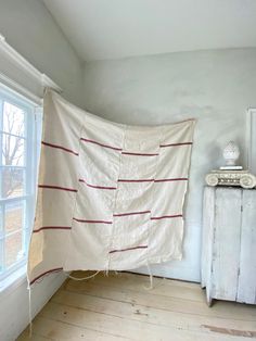 a room with white walls and wooden floors has a large blanket hanging on the wall