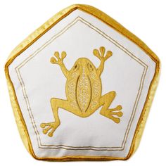 a yellow frog embroidered onto a white and gold hexagonal pillow with an intricate design