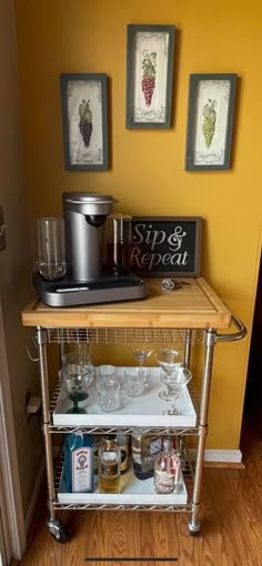 a kitchen cart with wine glasses and other items on it in front of a yellow wall