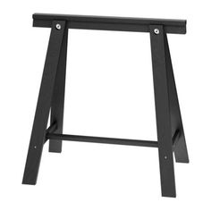 a black wooden stool sitting on top of a white floor next to a table with two legs