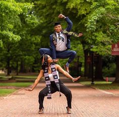 two people doing acrobatic tricks in the middle of a brick walkway near trees