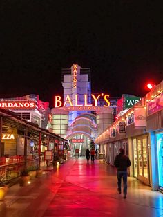 people are walking down the street in front of some shops at night time with neon lights