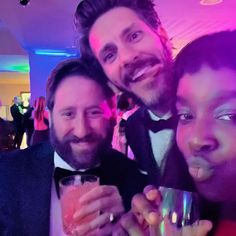 two men and a woman pose for the camera with drinks in their hands at an event