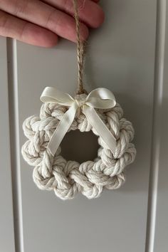 a hand holding a white rope ornament with a bow on the front and side