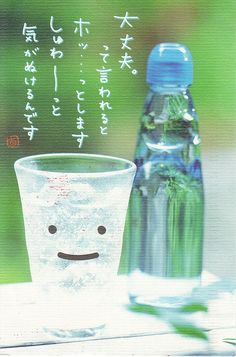 there is a glass cup with water in it next to a bottle that has an emoticive face on it