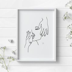 two hands touching each other in a white frame on a wall next to some flowers