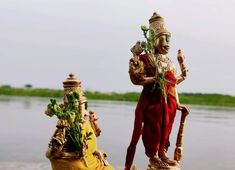 two statues are standing next to each other near the water's edge with plants growing out of them