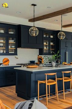 a large kitchen with black cabinets and wooden floors is pictured in this image, there are stools at the center of the island