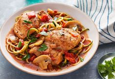 a white bowl filled with chicken, pasta and veggies on top of a table