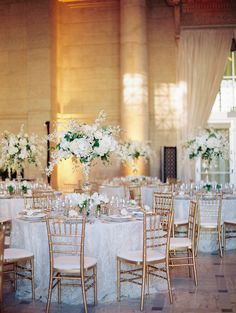 the tables are set with white flowers and gold chairs