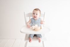 a baby sitting in a white high chair eating cake