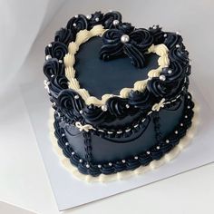 a heart shaped cake with black frosting and pearls on it's edges, sitting on a white surface