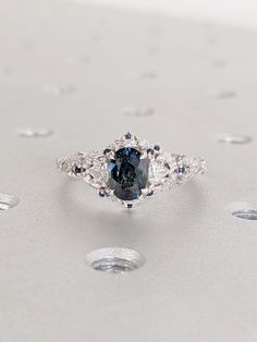 a blue diamond ring sitting on top of a white surface with drops of water around it