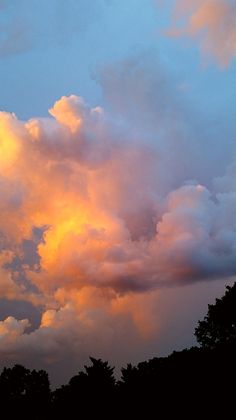 the sky is full of clouds as the sun sets over some trees in the distance