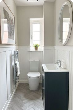 a white toilet sitting in a bathroom next to a sink under a mirror and a window