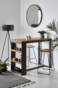 a table with two stools next to a mirror and potted plant in a white room