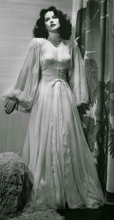 an old photo of a woman in a long dress standing next to a curtain with her hands on her hips