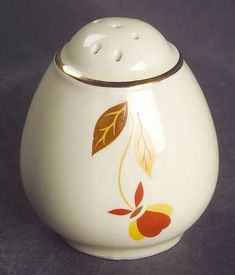 a white ceramic jar with an orange and yellow leaf design on the front, sitting on a gray surface